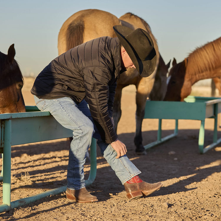 A cowboy wearing Justin Boots Ante Up 13-inch Western Boots in Hickory brown. Shop Ante Up.