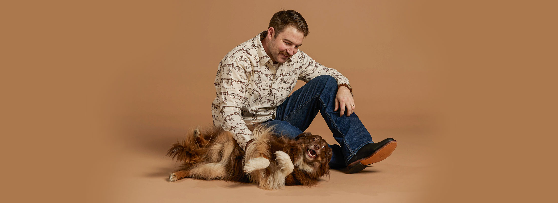 A man sitting on the floor with a dog wearing Justin Jeans.