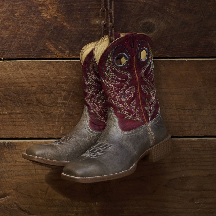 Men's Pickett 11” western boot in red and grey being hung by a chain on a wood background.