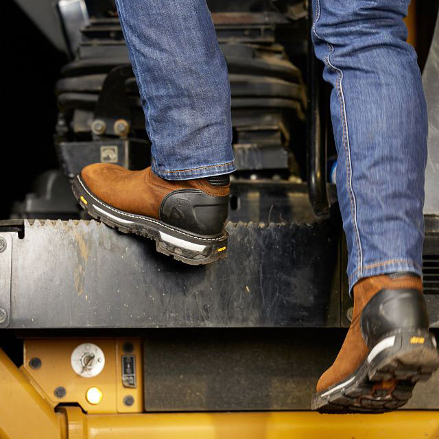 A man wearing Justin Boots' Frontline HiViz 11” Waterproof Work Boots in Walnut color climbs up the steps of heavy machinery. Shop Frontline HiViz.