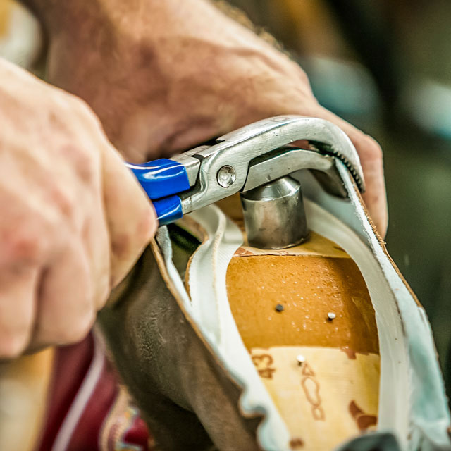 Worker stretching leather over a boot form (last).