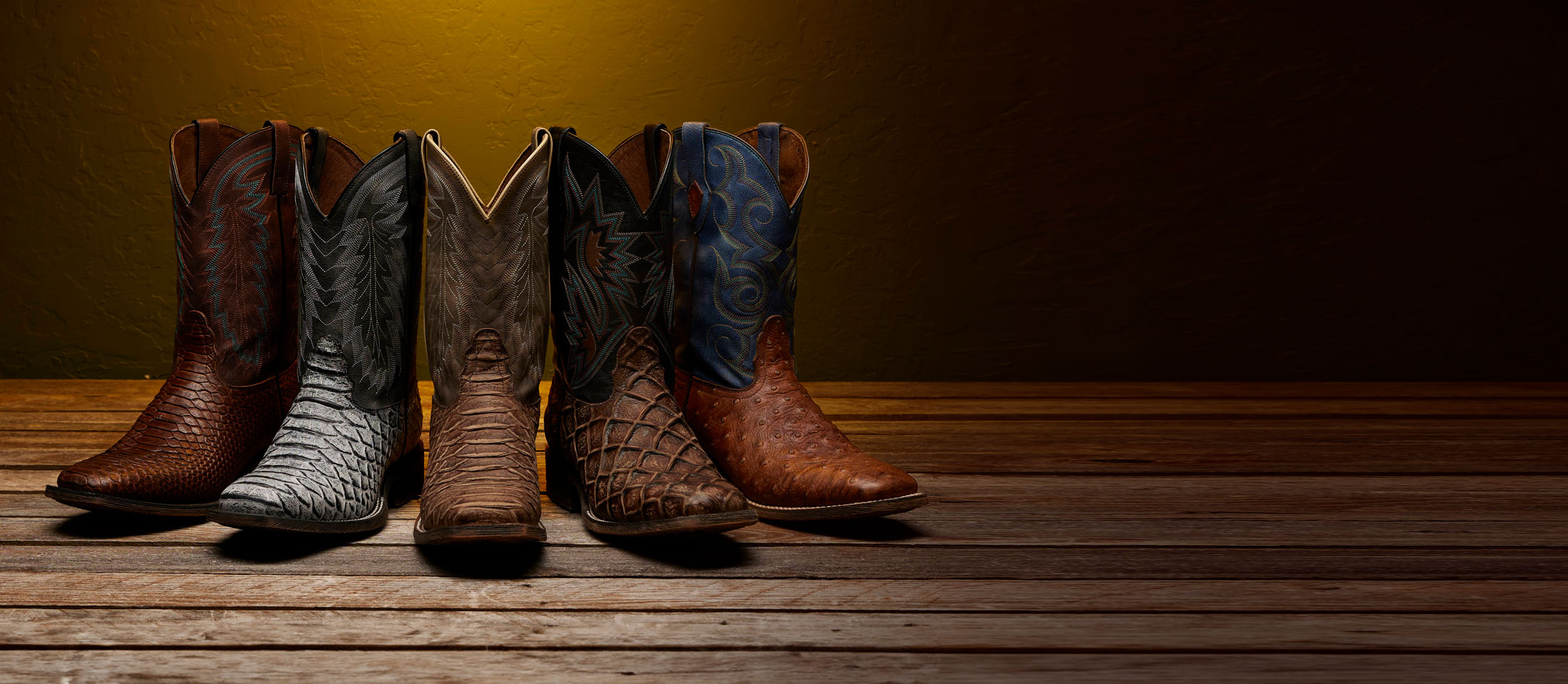 5 mens boots on a wood floor with a light shining above