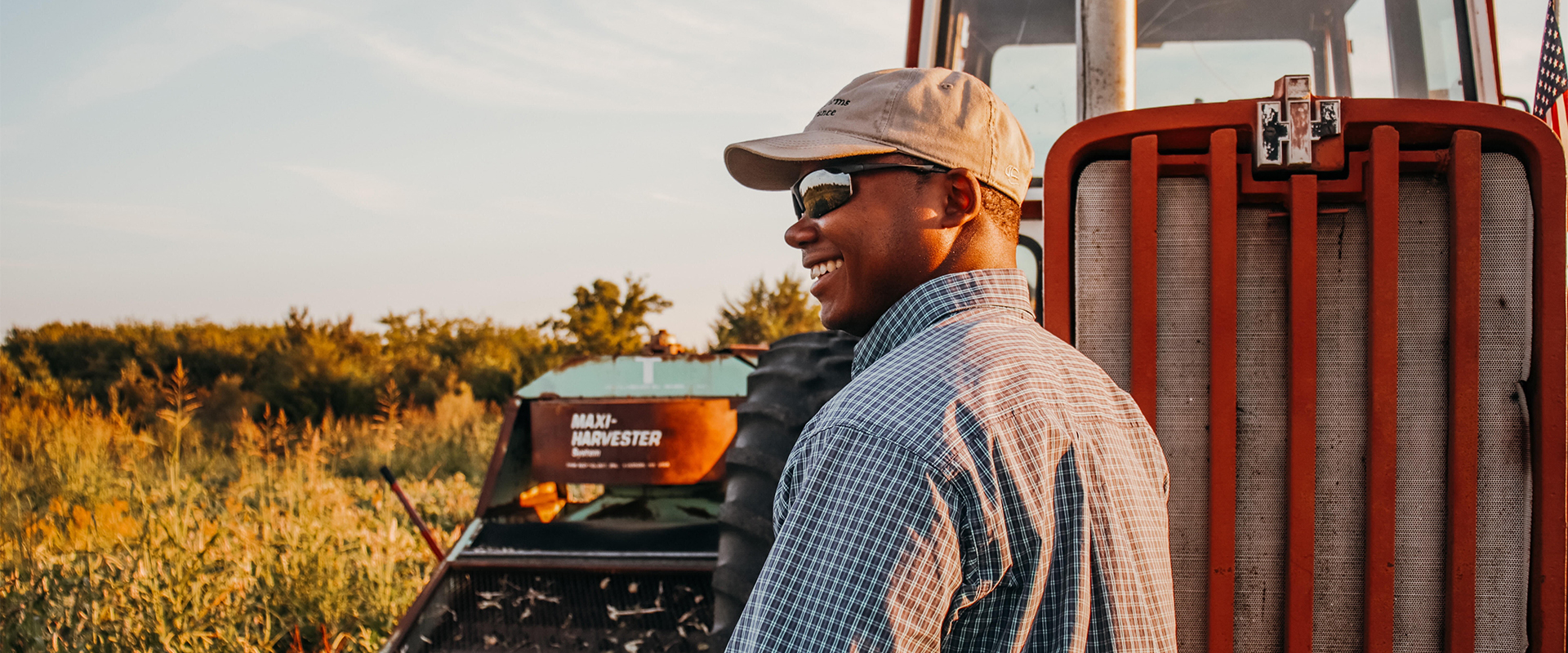 Terren outside in front of tractor wearing a button up shirt, sunglasses and hat.