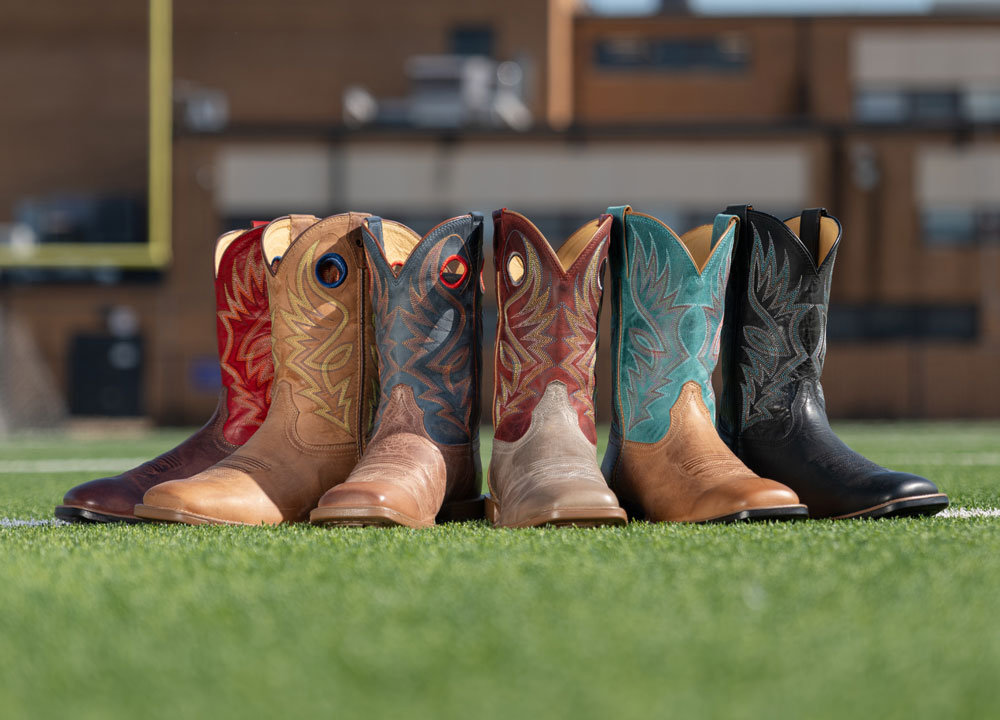 A group of Justin Untamed western boots displayed on a turf field.