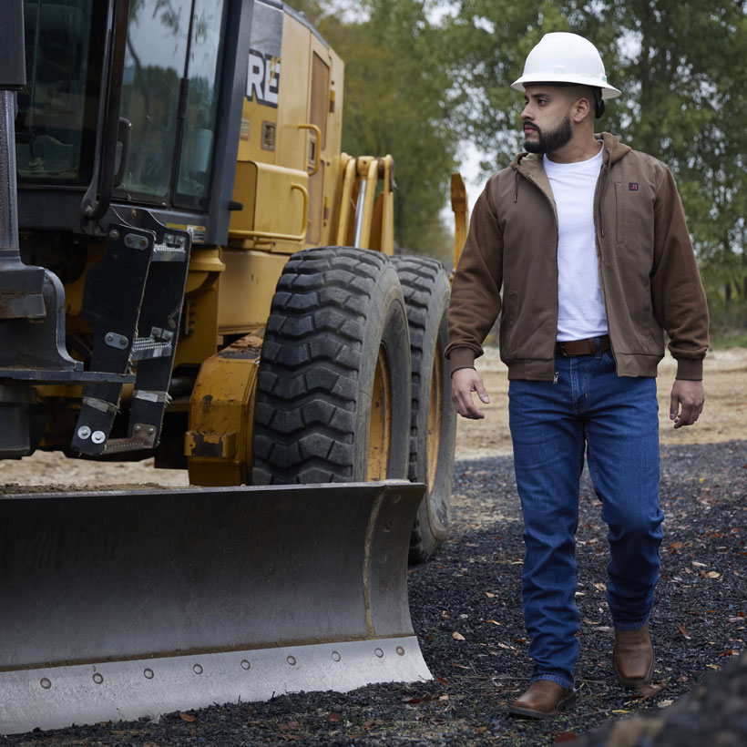 A man wearing Justin Work Boots while standing next to a tractor.