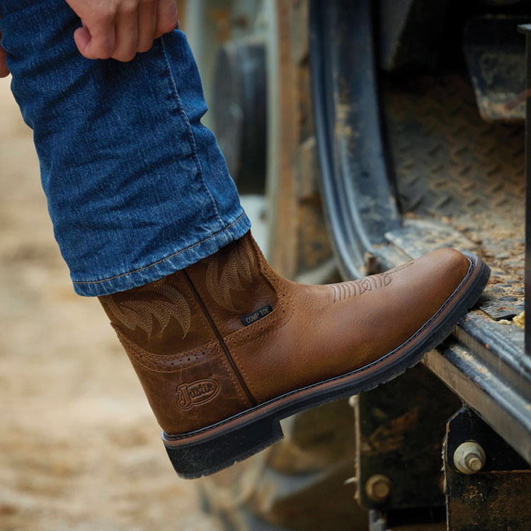 Close-up of a person wearing Justin Boots Handler 11-inch Comp Toe boots in brown. Shop Handler.