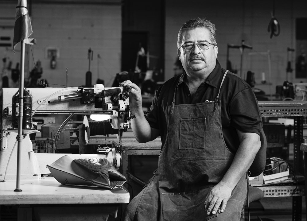  A hispanic man standing next to shoe making equipment.