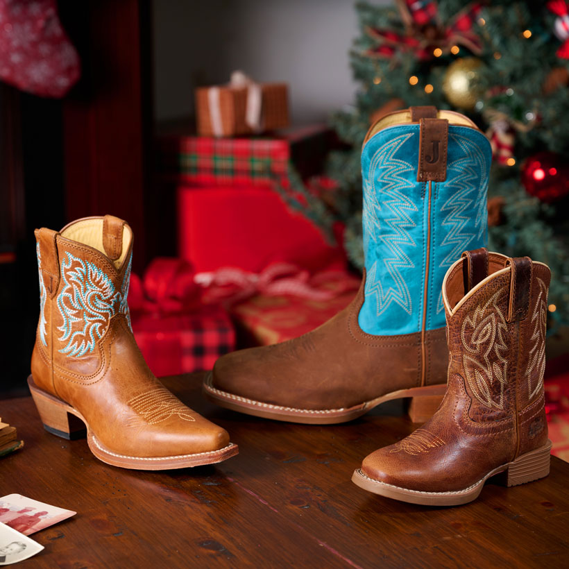 Canter Junior in Amber Brown, Jackpot 11" Western in brown, and Isabella 7” in tan cowboy boots posed on a table with a Christmas scene behind them.