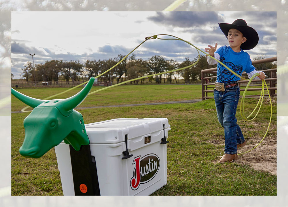 Un niño con sombrero de vaquero lanza un lazo alrededor de un toro falso.