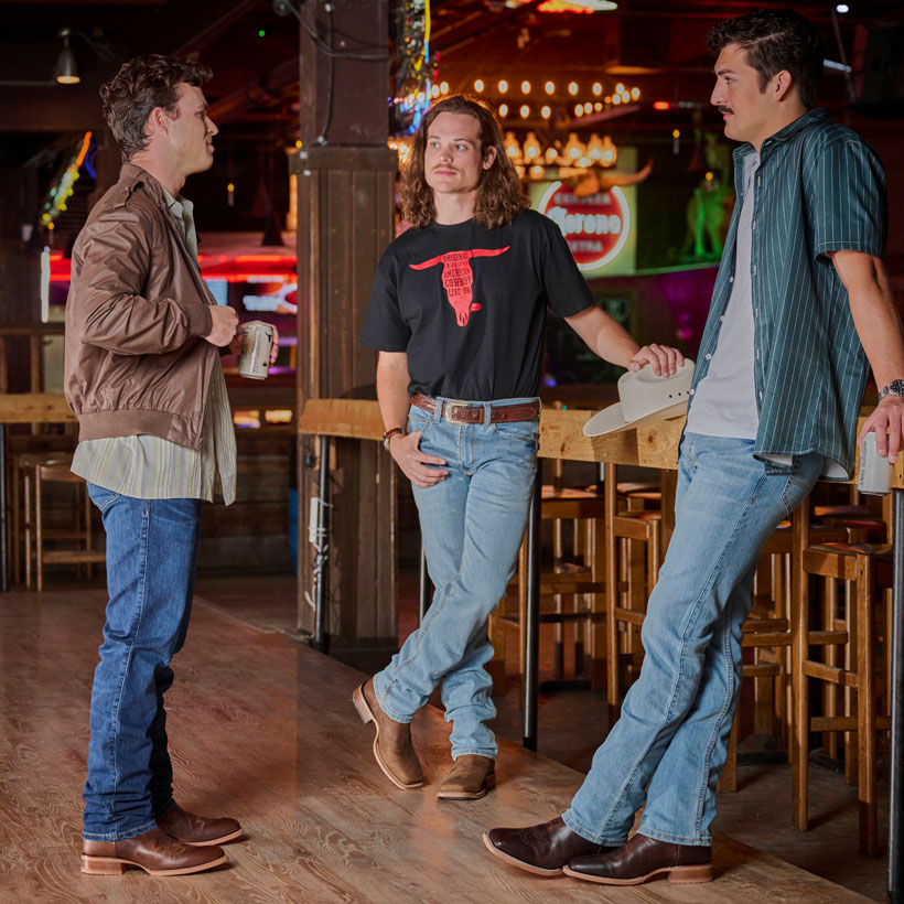 Men’s 1879 Straight-leg men’s jeans in dark wash and light wash worn by three guys with dark hair standing at the bar. 