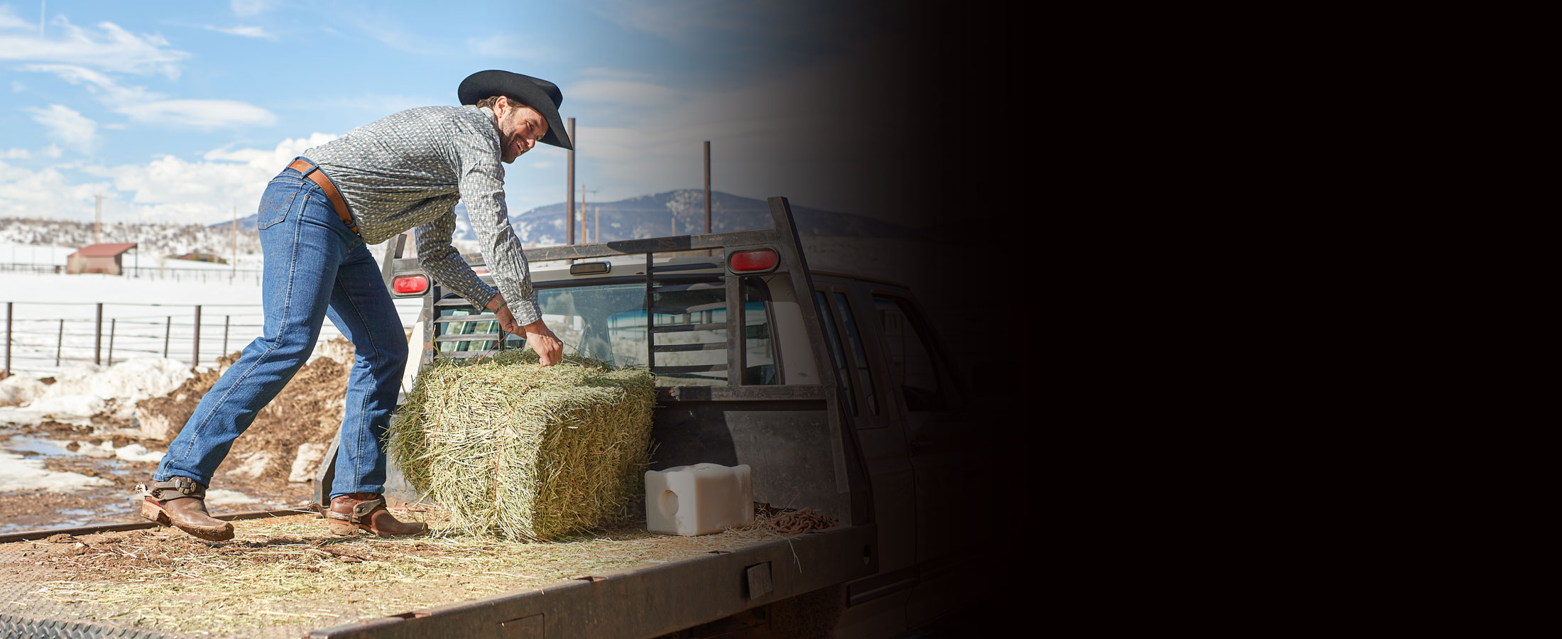 A man wearing Justin western boots while lifting a bale of hay onto the back of a truck.