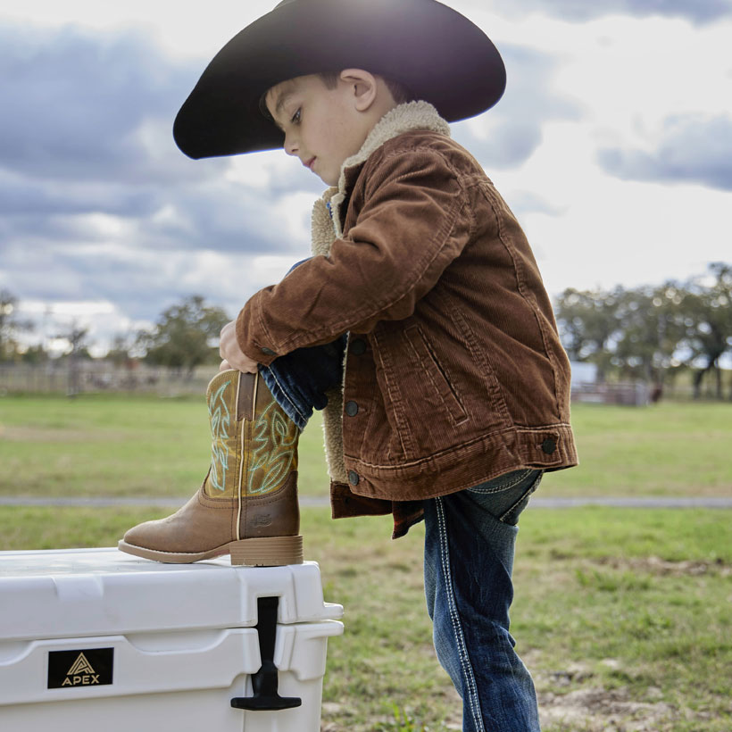 A small child wearing Canter Junior in Clay Brown and a cowboy hat showing off his boots.