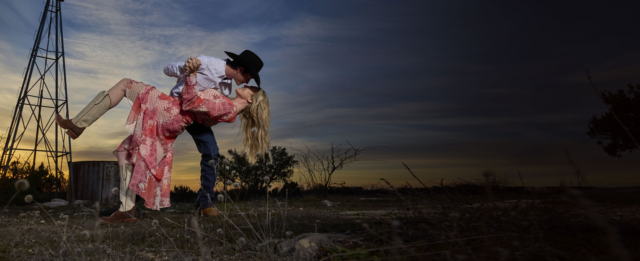 A woman wearing Justin Women’s Wrap Maxi Dress in red and a man wearing show off 13” western boot in tan. 