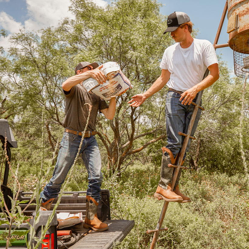 Men’s Rush Strike 17” Snake Resisting boots being worn by two men climbing a ladder in a field.