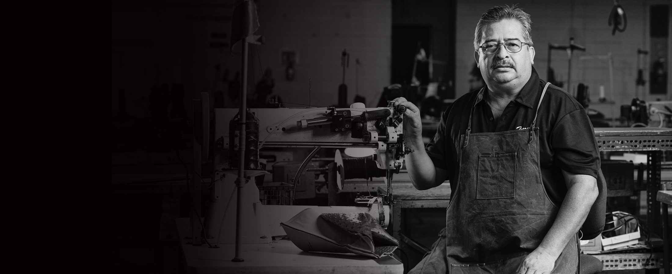  A hispanic man standing next to shoe making equipment.