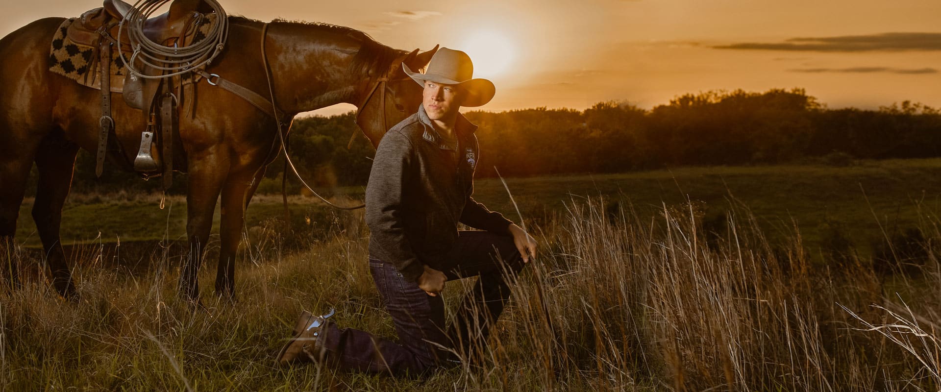 cody con sombrero de vaquero se arrodilla en el campo frente a un caballo