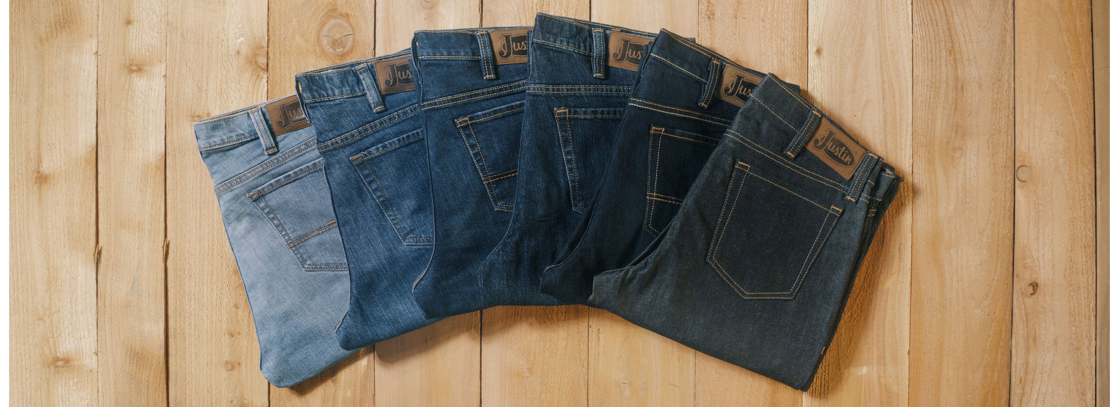 A fan of different washes of jeans ranging from light to dark denim laying on a wood background.