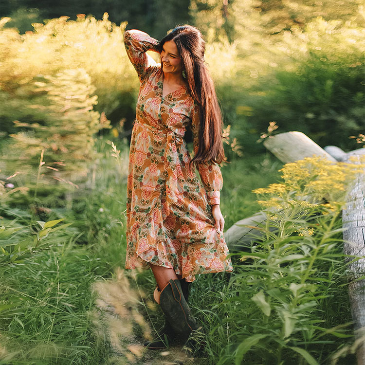 Justin Women’s Wrap Maxi Dress in Green Floral, worn by a woman with brown hair, posing in a green field of flowers.