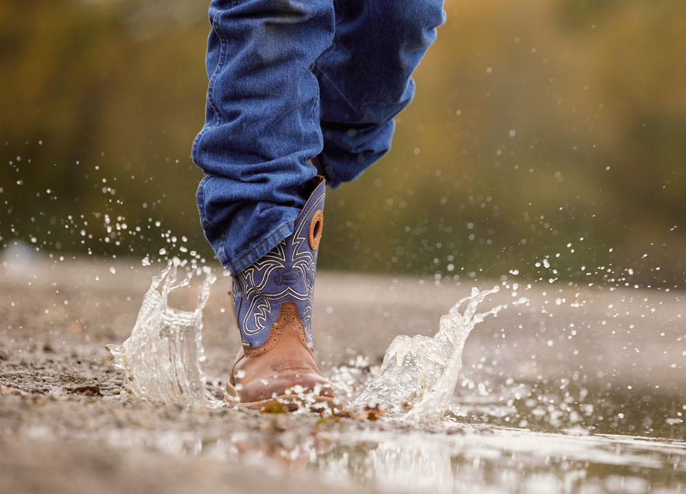 A man wearing Justin Waterproof work boots while walking through a puddle.