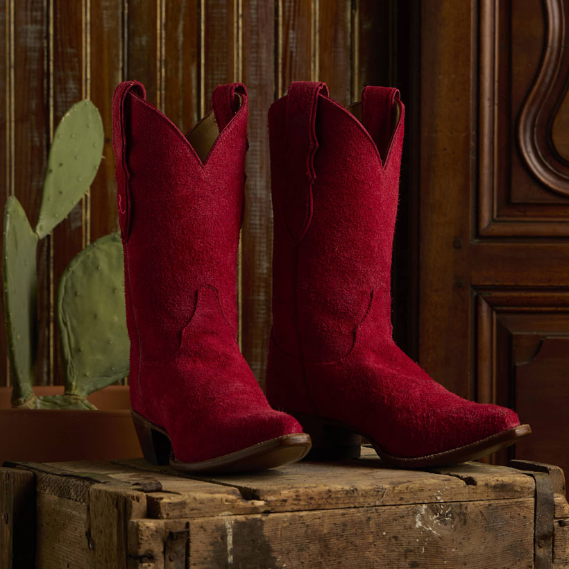 Women's Fancy 11" Suede western boot in red posed next to a green cactus and sitting on a brown trunk.