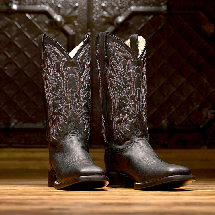 A pair of Justin Boots Three Bars Smooth Ostrich cowboy boots in Black, standing on a wooden floor. Shop Three Bars Smooth Ostrich.