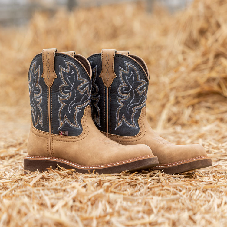 A pair of Justin Boots Kay 8-inch Western Boots in Honey, displayed on a bed of straw. Shop Kay.