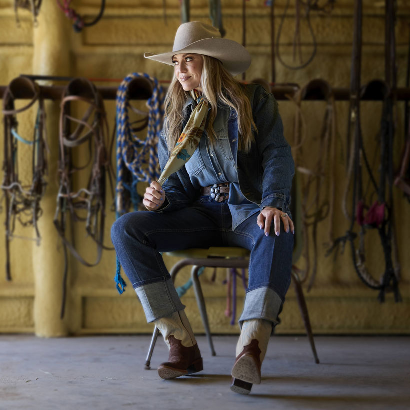 A woman in western clothing wearing the Clara 15" Western Boot in white and brown.