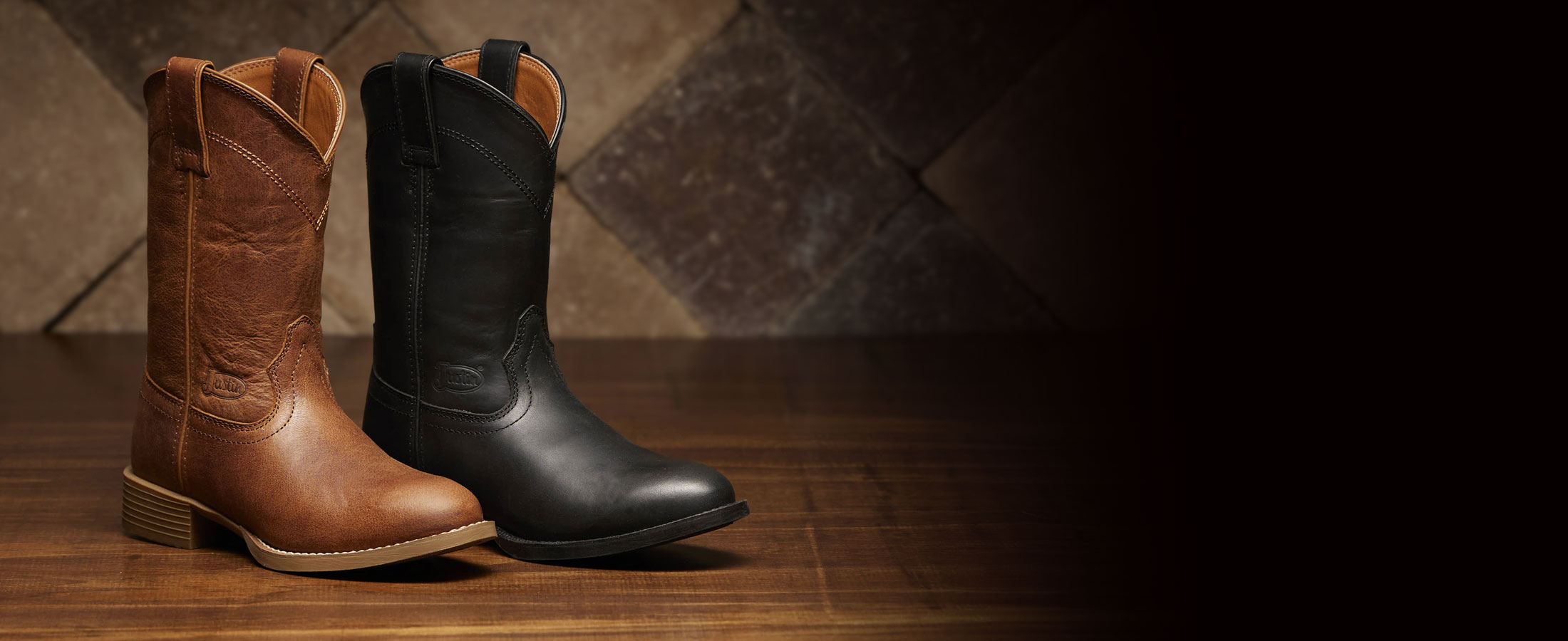 A Justin Stampede Roper in brown and a Justin Stampede Roper in black on a wood floor.