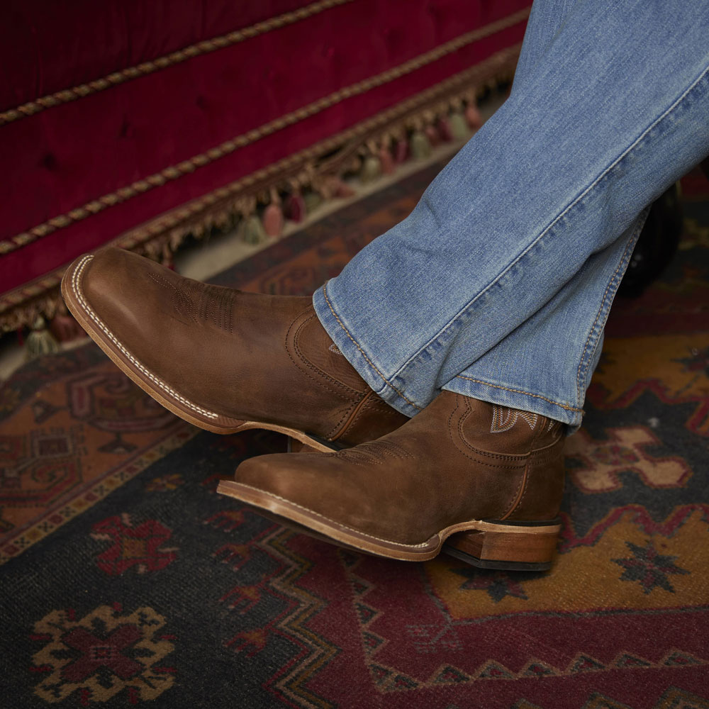 A man wearing the Justin Jackpot 11”Western boot in brown. Shop Jackpot