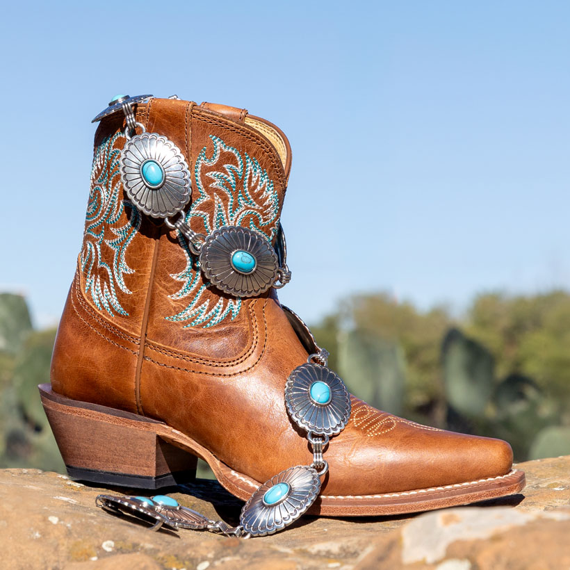 Women’s Isabella 7” Bootie in brown, posed on a rock with Farmington Classic Chain Belt posed on top of the boot.