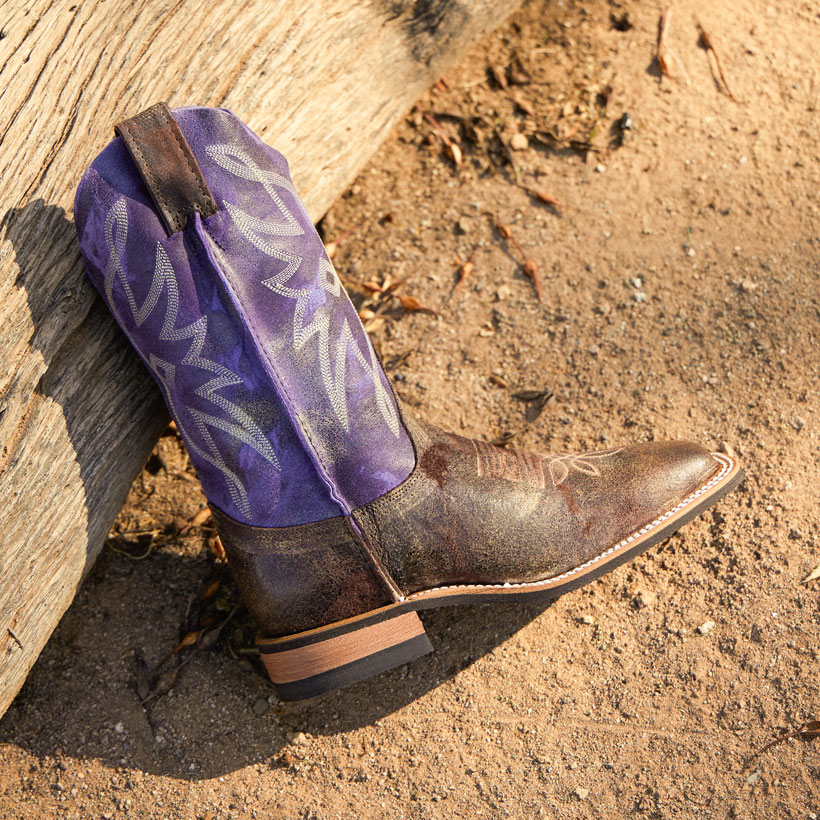 Women’s Sterlington 11” Western Boot in purple and brown, laying down on the ground in the dirt. 