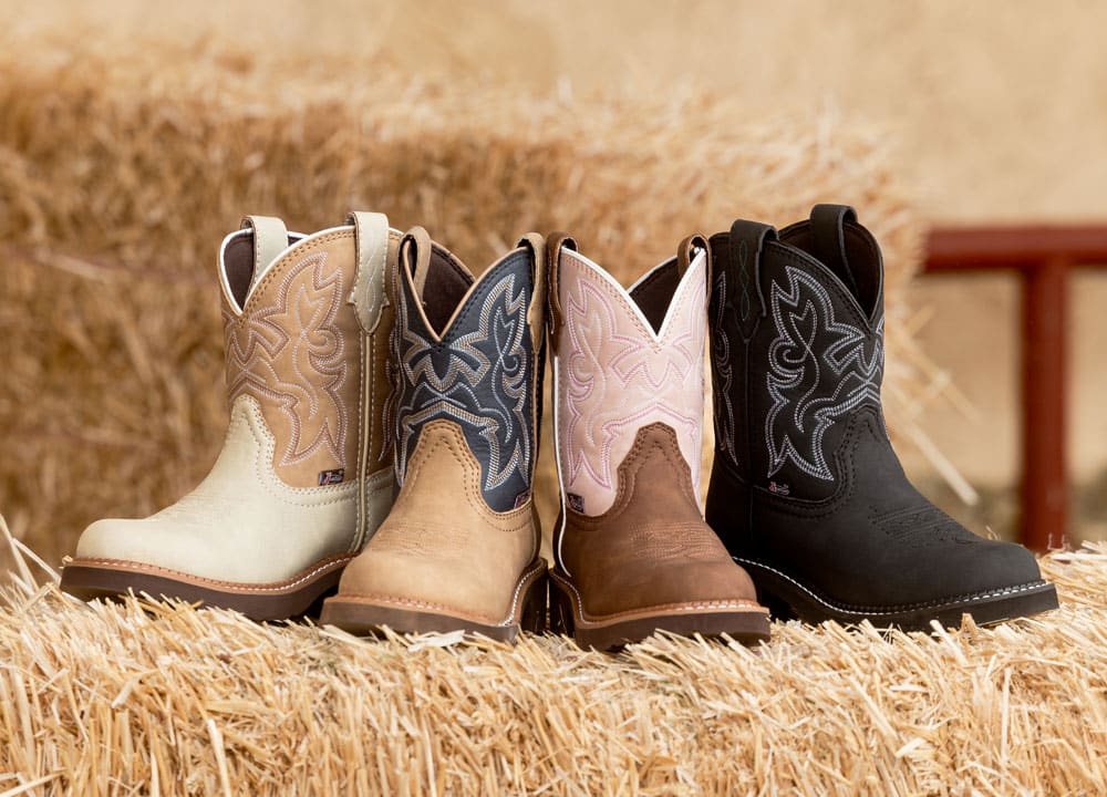 Kay 8” Western boots in brown and black posed on a hay bale at a cattle barn.