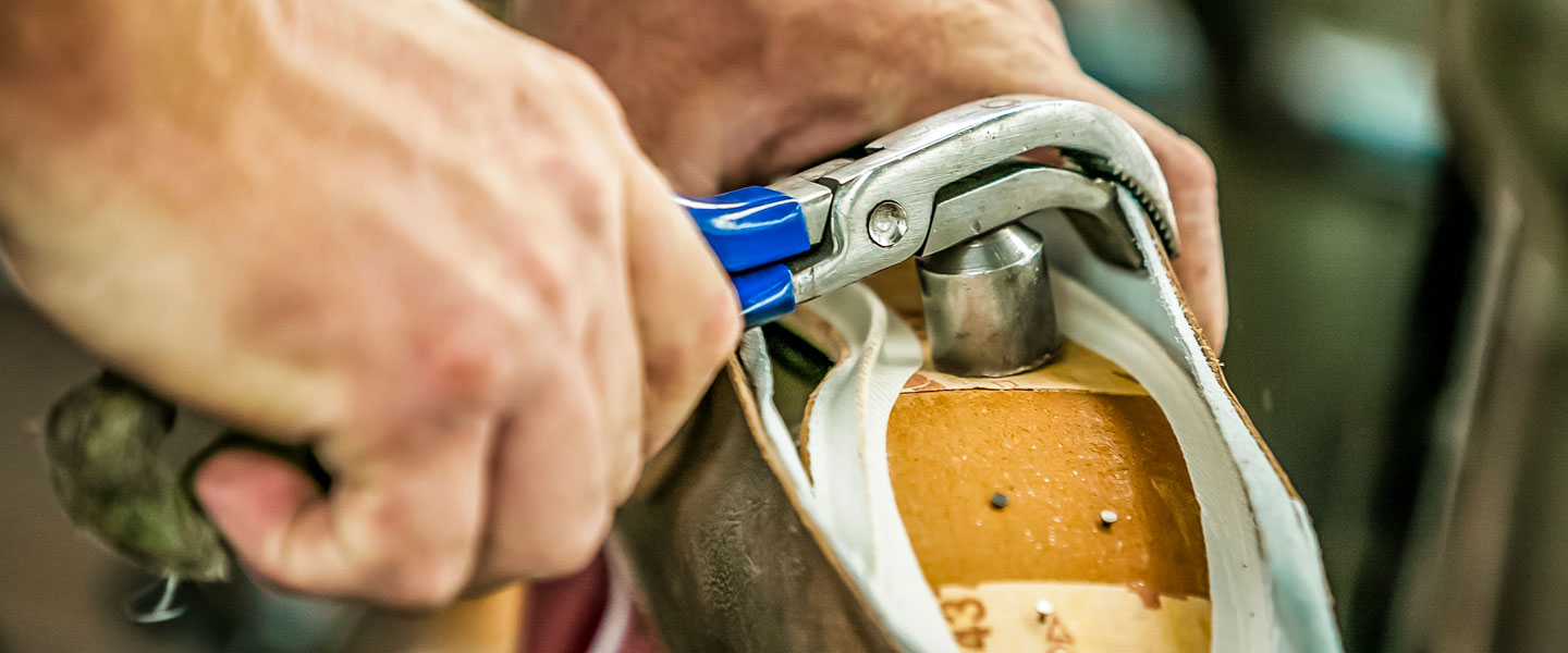 Worker stretching leather over a boot form (last).