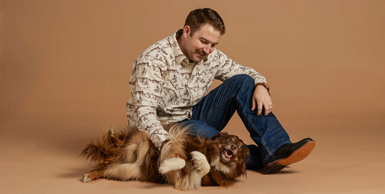 A man sitting on the floor with a dog wearing Justin Jeans.